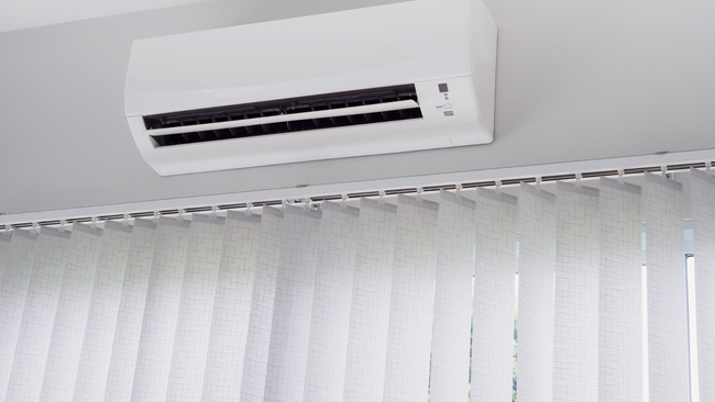 White wall-mounted air conditioner above white vertical blinds