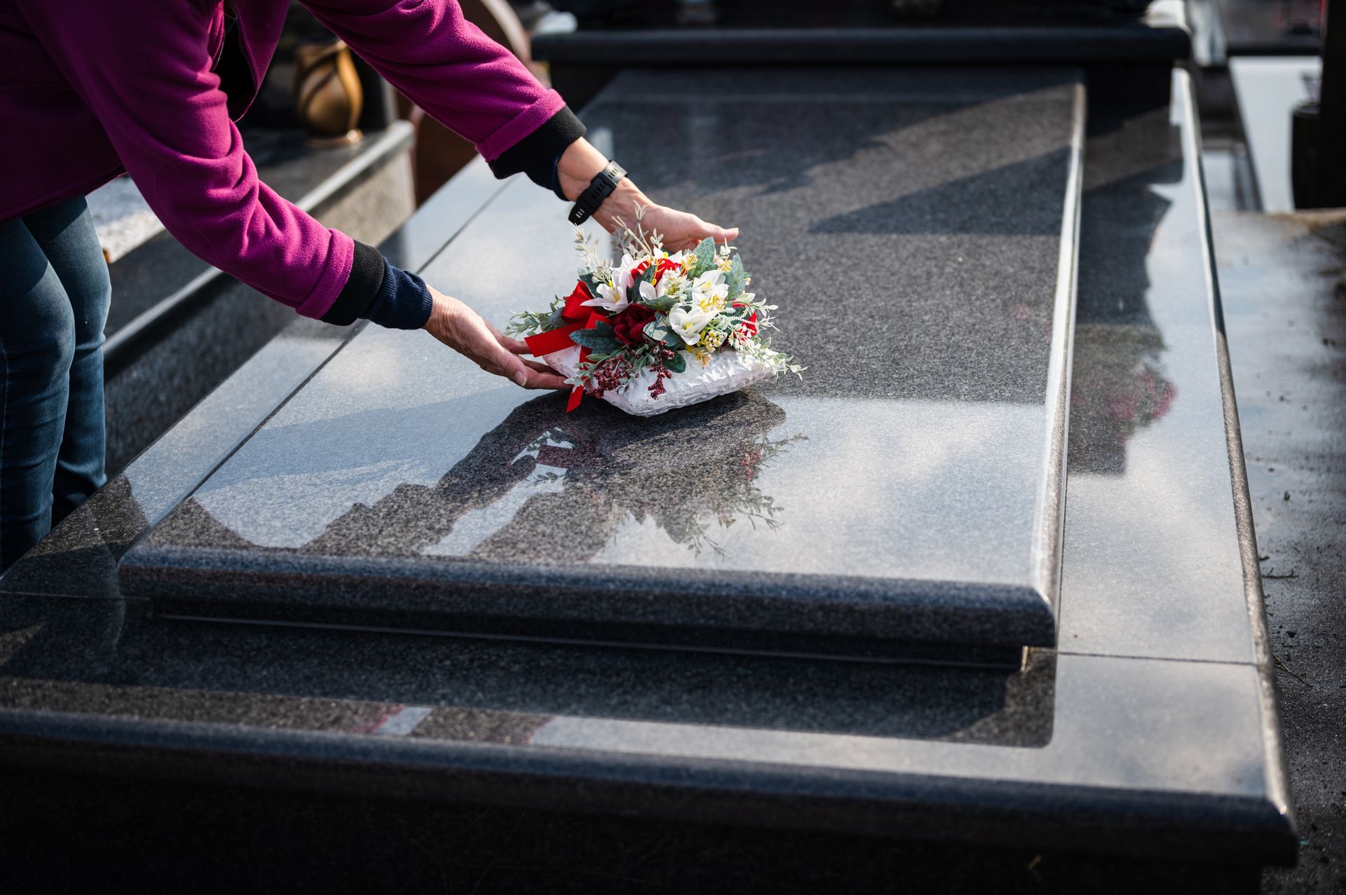 Woman placing flower bouquet on granite gravestone, mourning and remembrance concept.