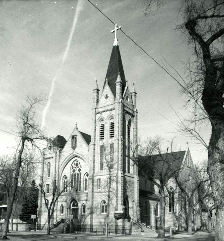 Black-and-white photo of a Gothic-style church with a tall steeple and bare trees nearby