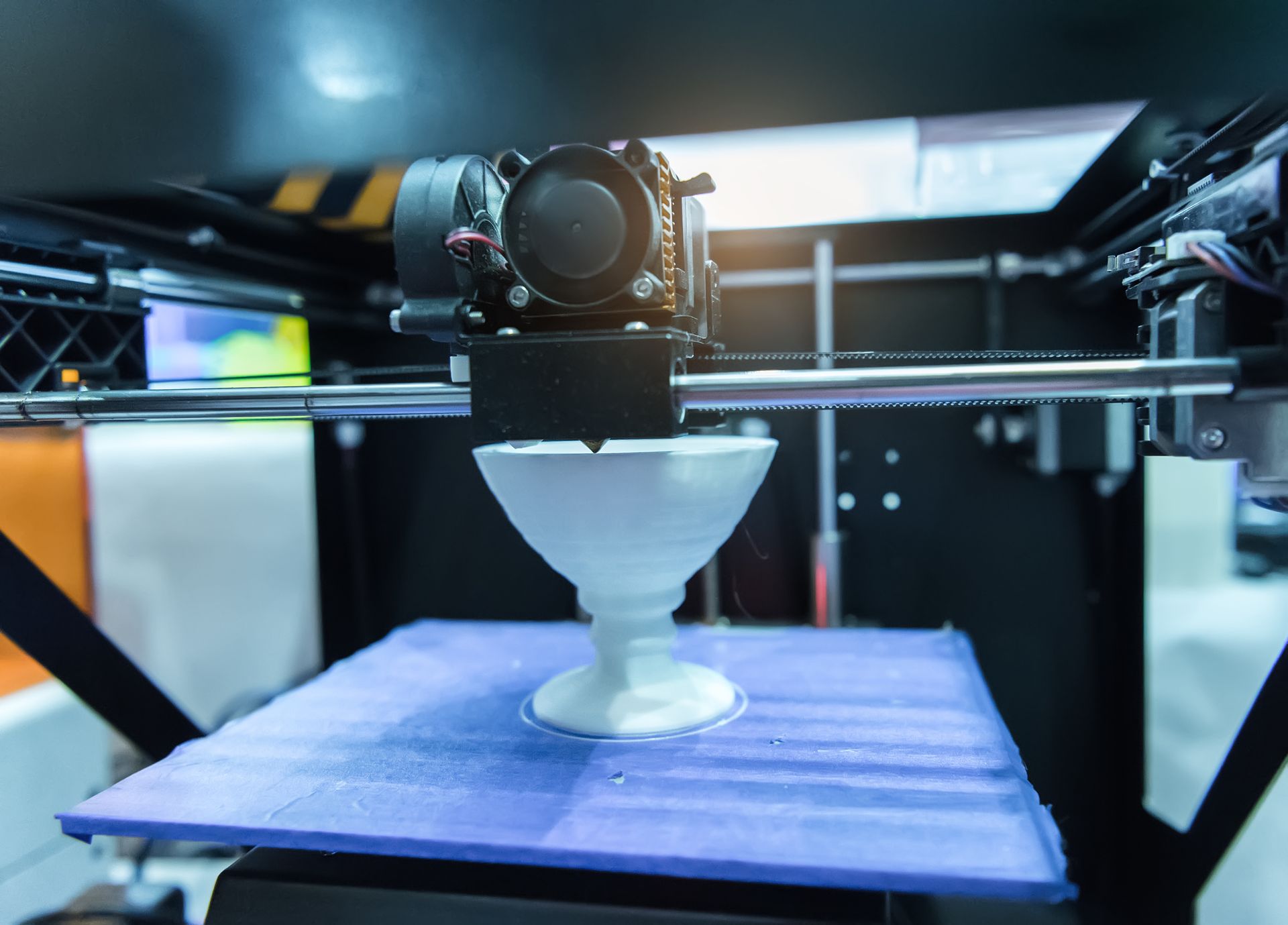 Ein 3D-Drucker druckt ein weißes Objekt auf eine blaue Bauplatte.