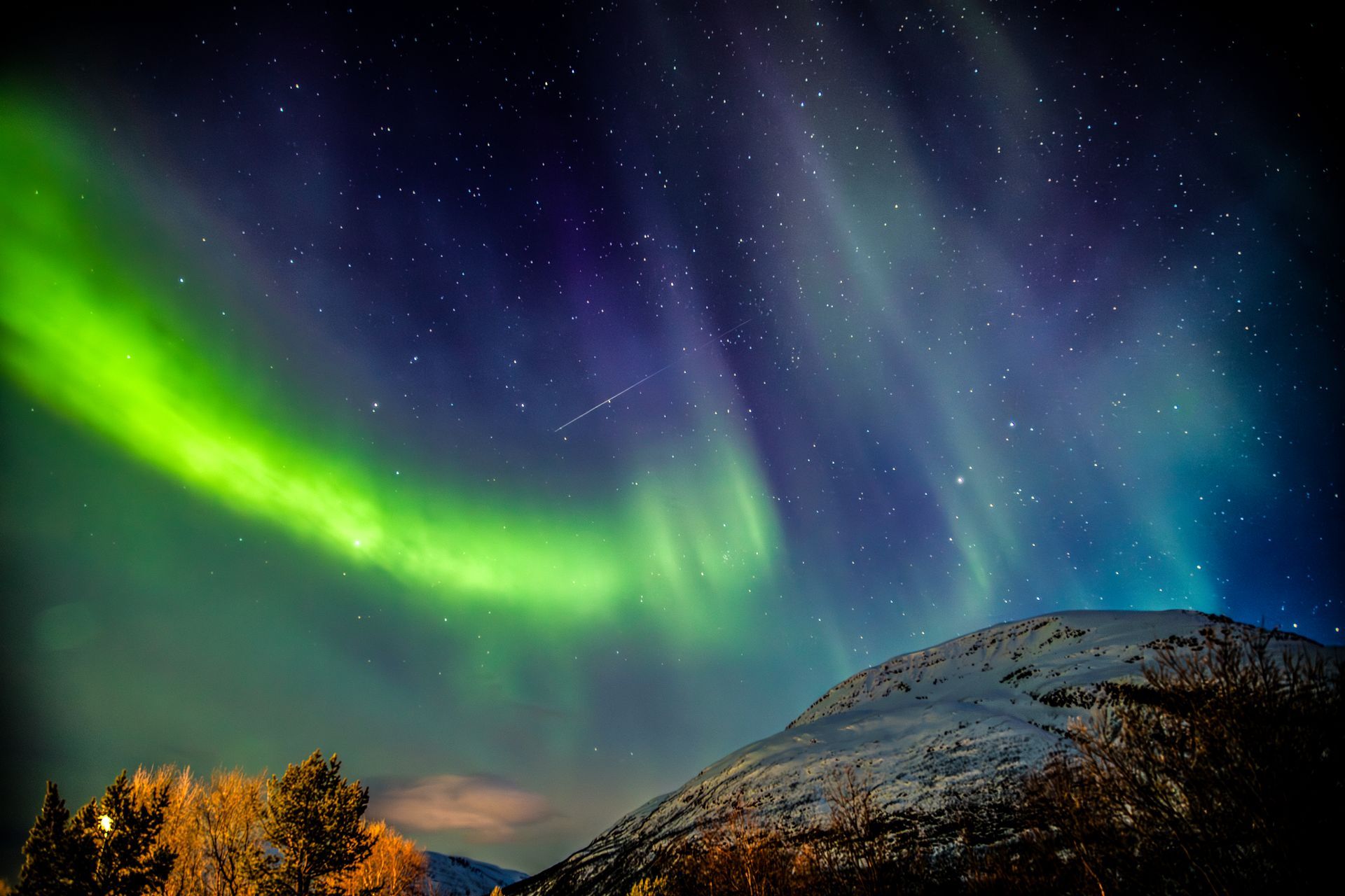 Grüne Polarlichter erleuchten den sternenklaren Nachthimmel über einem schneebedeckten Bergkamm.