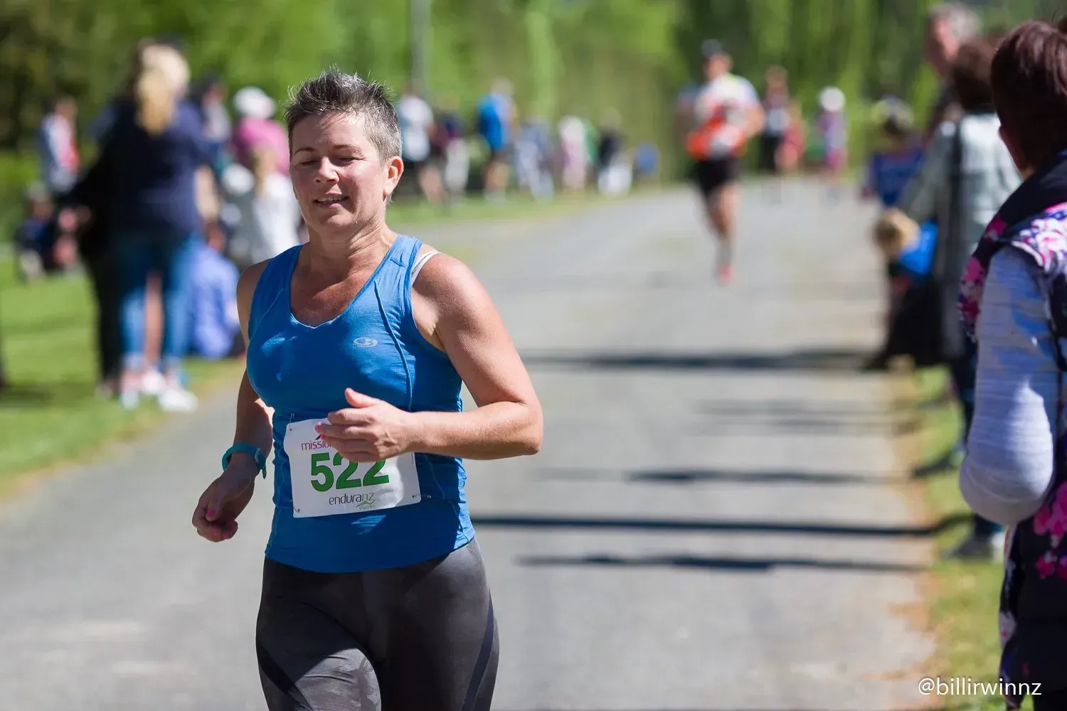 A woman in a blue tank top is running in a race.