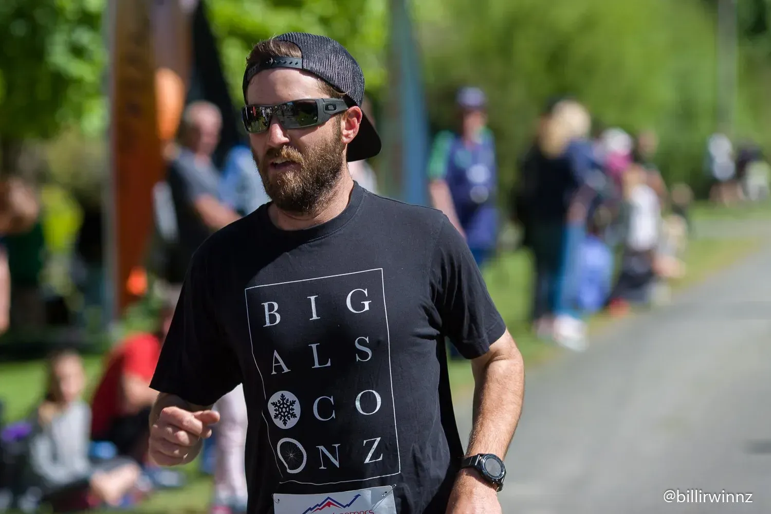 A man wearing sunglasses and a hat is running in a park.