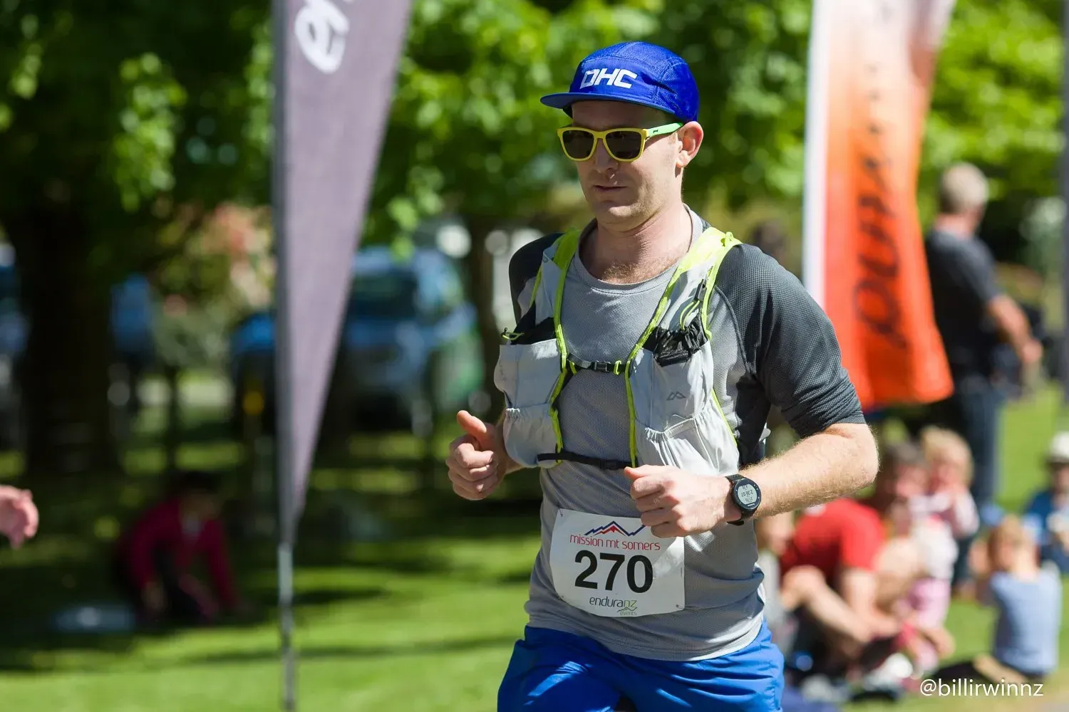 A man wearing sunglasses and a hat is running in a park.
