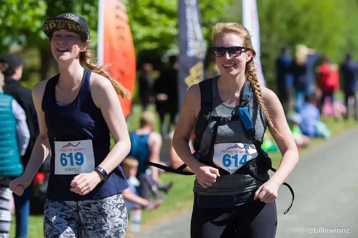 Two women are running in a race with numbers on their shirts.