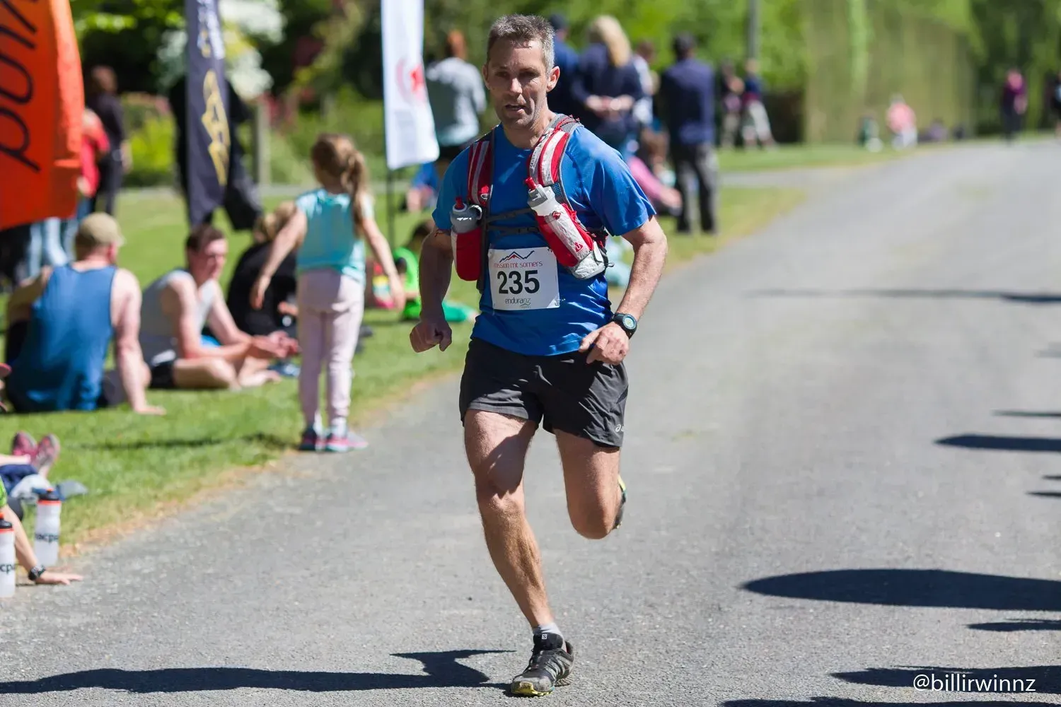A man wearing a blue shirt with the number 135 on it is running down a road.