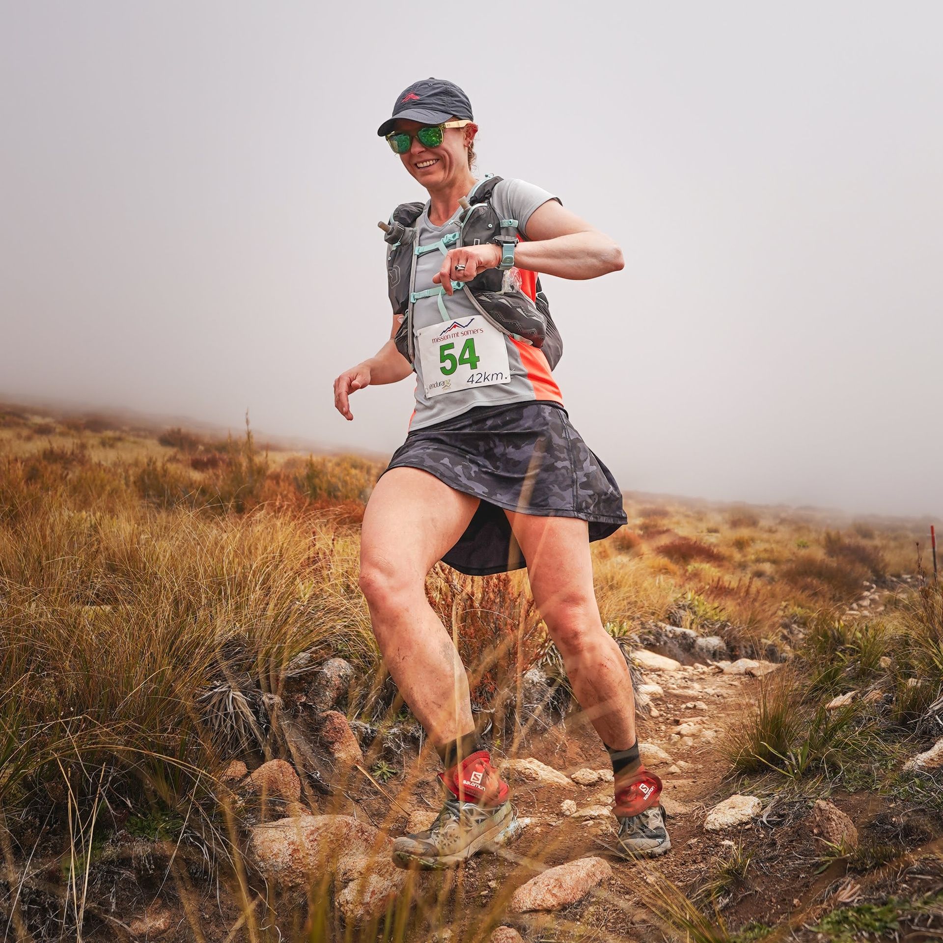 A woman is running on a trail with a number 54 on her shirt.