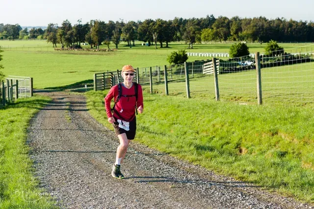 A man in a red shirt is running down a dirt road.