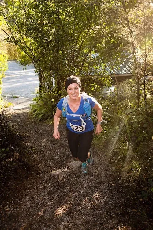 A woman is running down a trail in the woods.