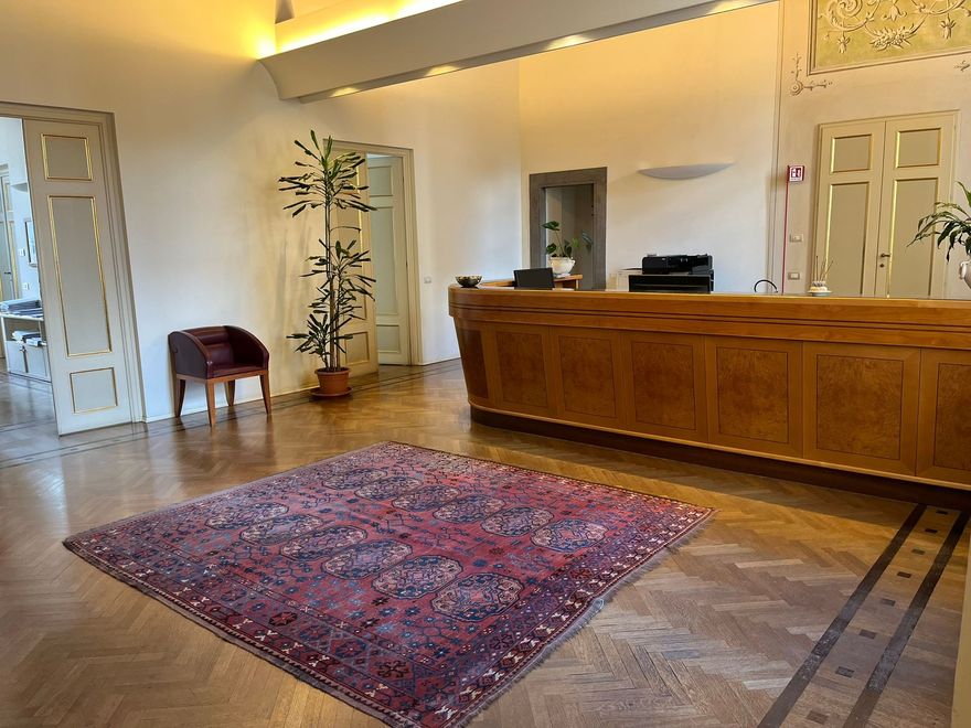 Un ufficio con una grande scrivania in legno, un divano rosso e una porta ad arco che conduce alla biblioteca.