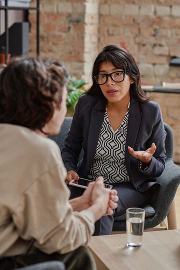 Woman in suit gestures while talking to someone. Brick wall background.