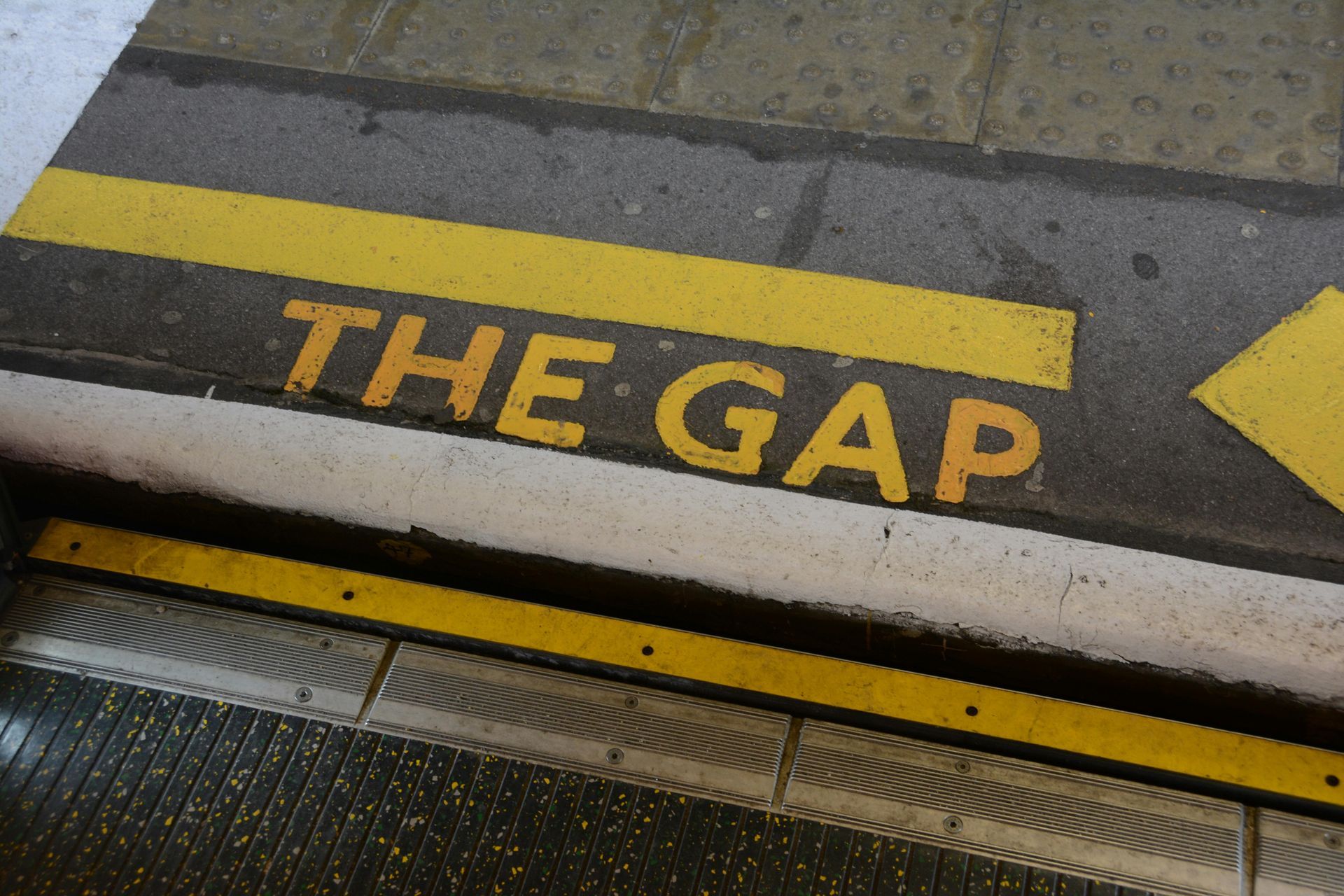 Yellow “THE GAP” marking on a train platform beside the edge and warning strip