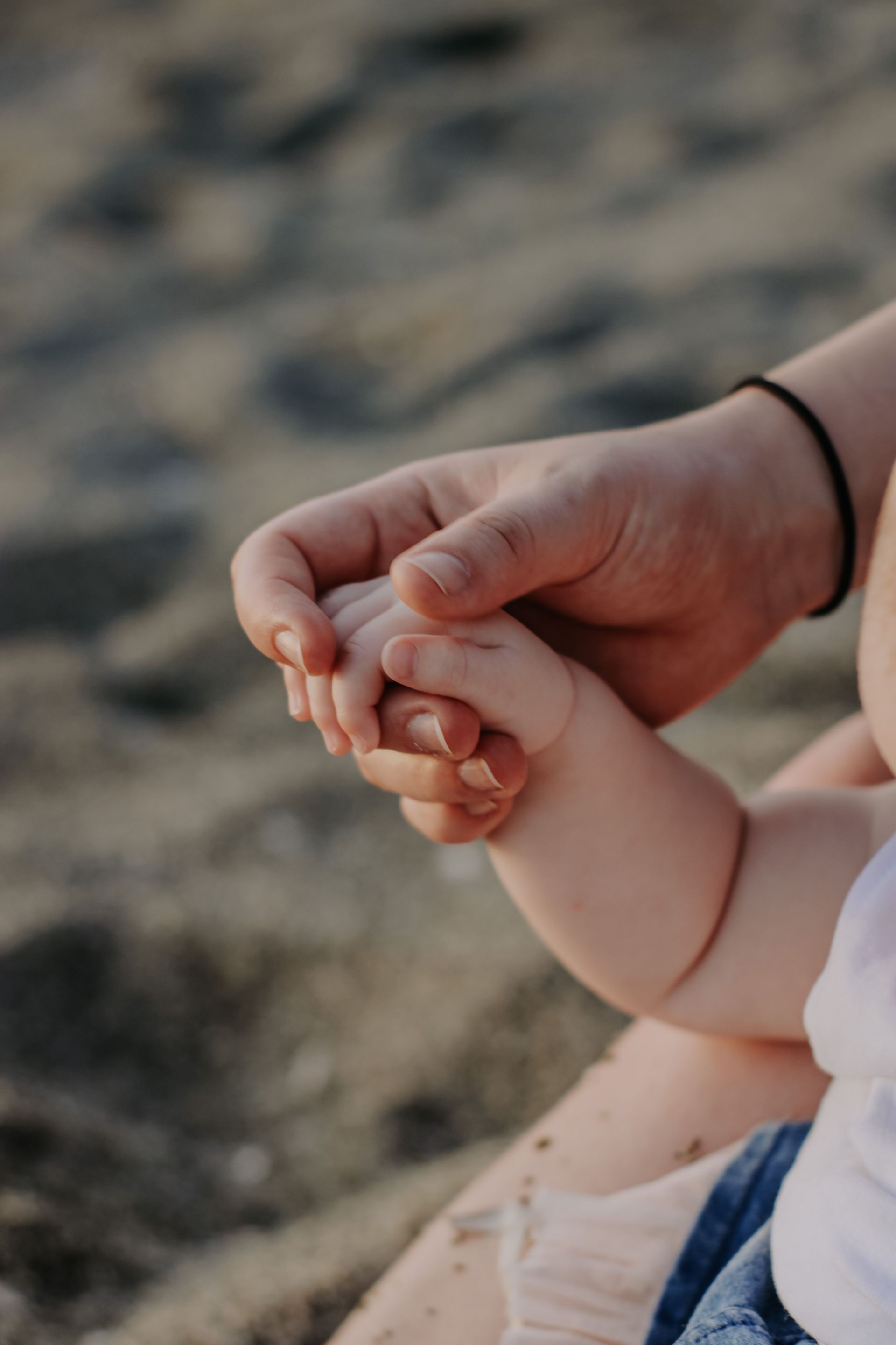 Two hands gently holding on a sandy beach, with a black bracelet visible on one wrist.