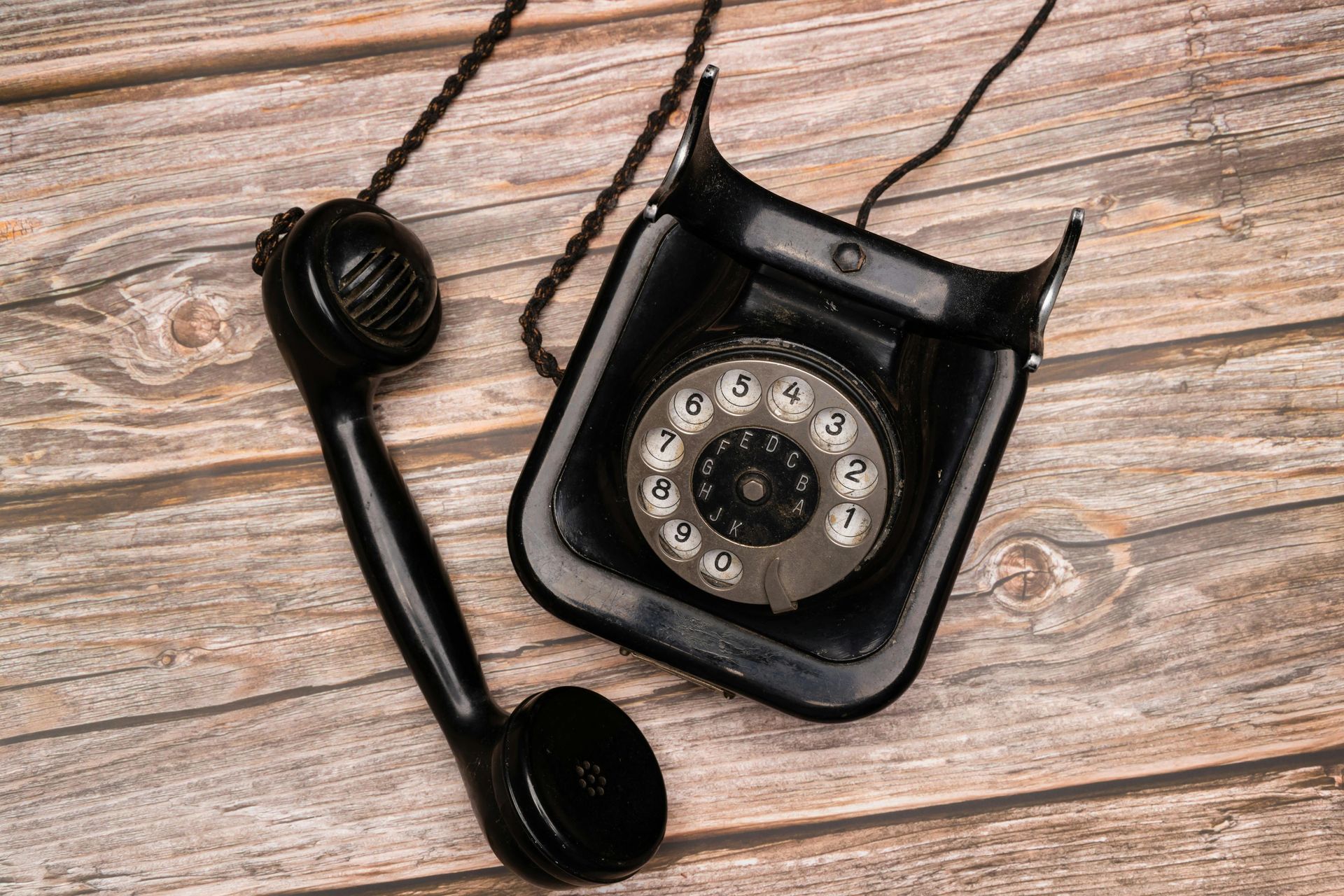 Black rotary telephone handset beside a vintage wall phone on weathered wood planks