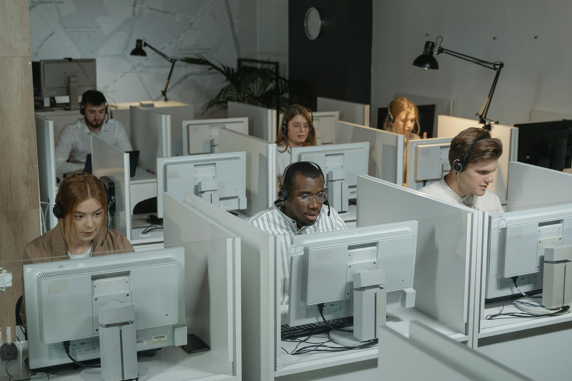 Office workers seated at computer desks in a row of cubicles, focused on their screens