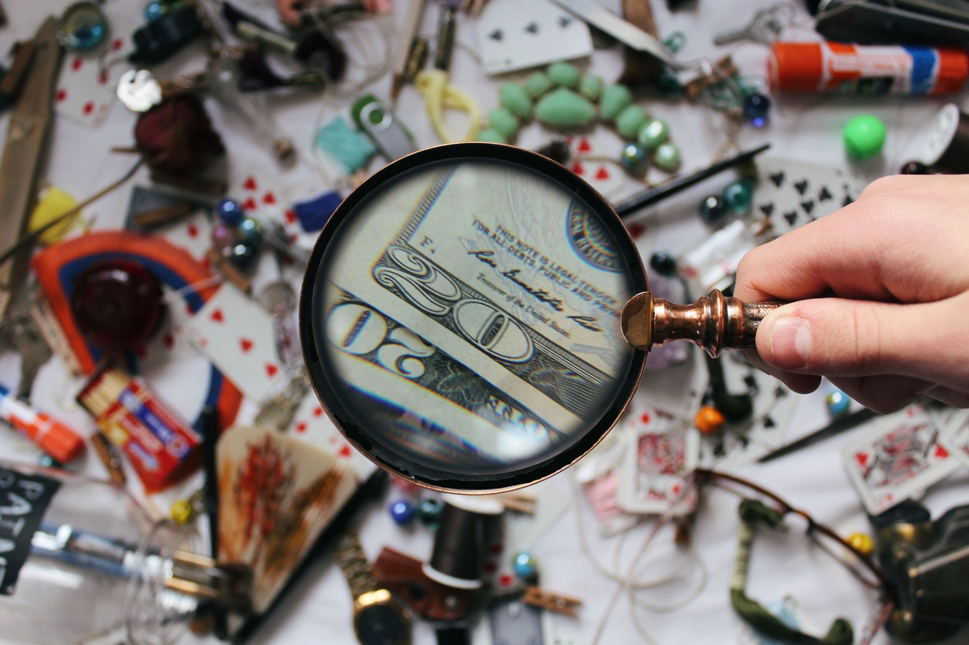 Hand holding magnifying glass over scattered tools and paper bills on a cluttered desk