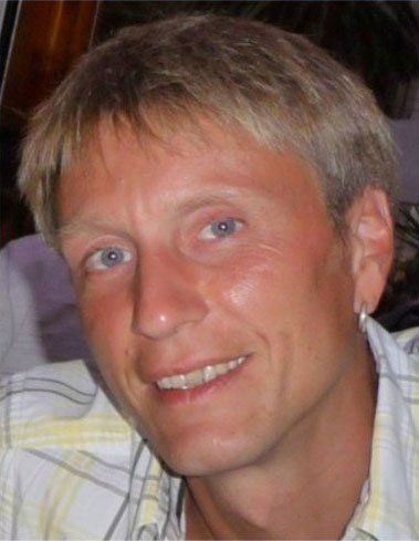 Nahaufnahme einer lächelnden Person mit kurzen blonden Haaren, die ein kariertes Hemd trägt.