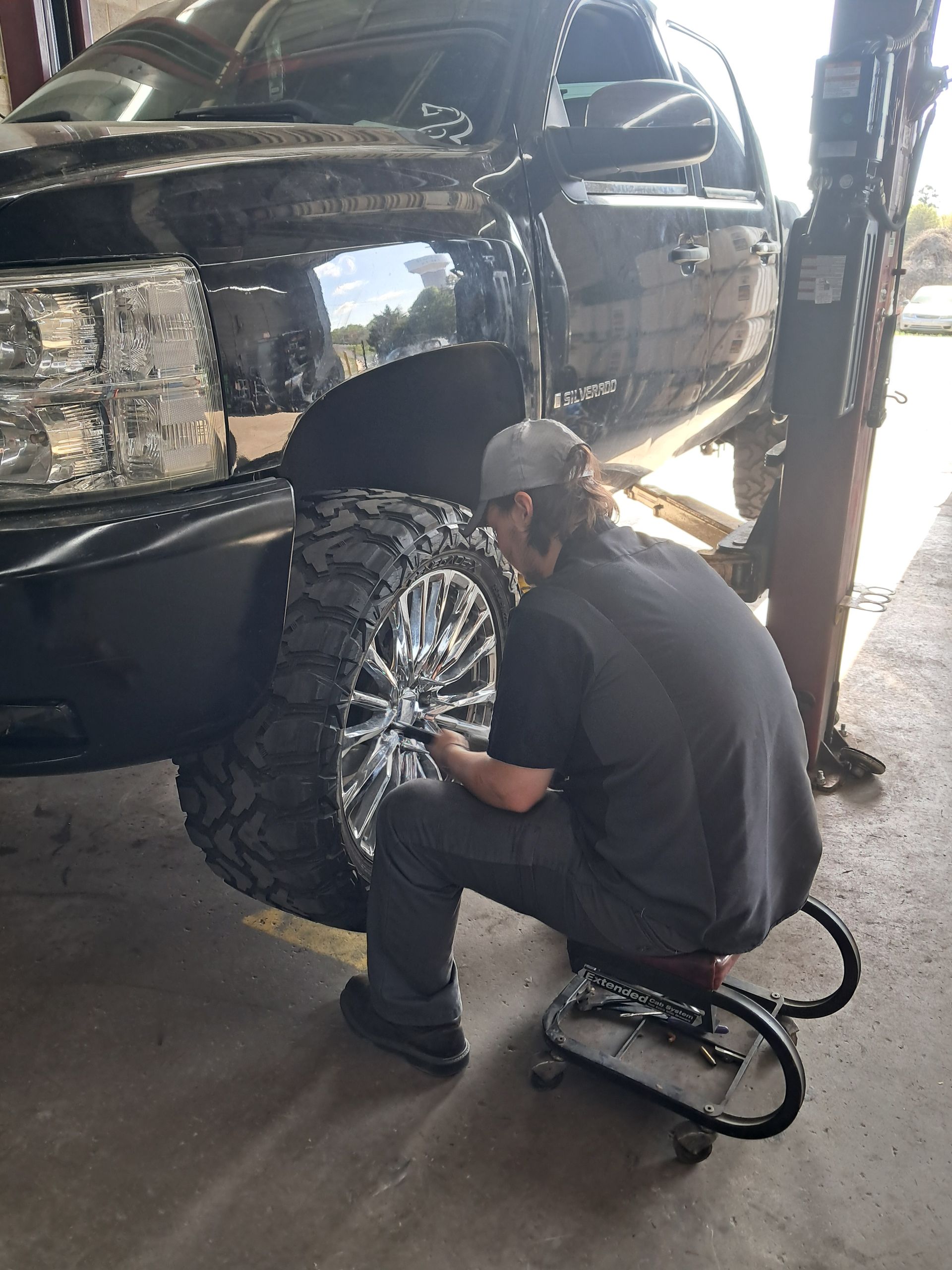 A wheel alignment target sensor mounted to the alloy rim of a car tire on an auto repair shop lift.