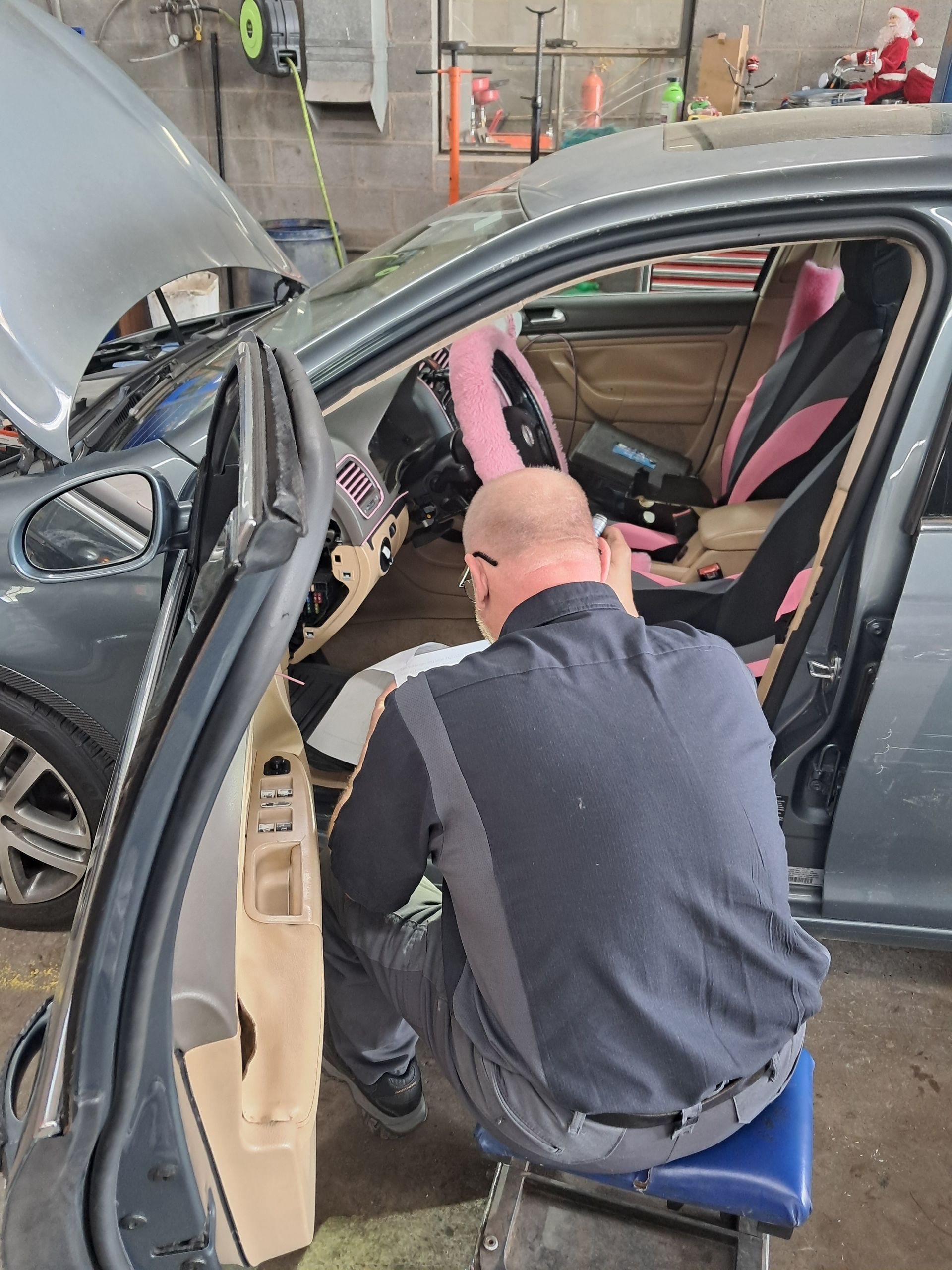 A person wearing work gloves using red jumper cables to jump-start a car battery .