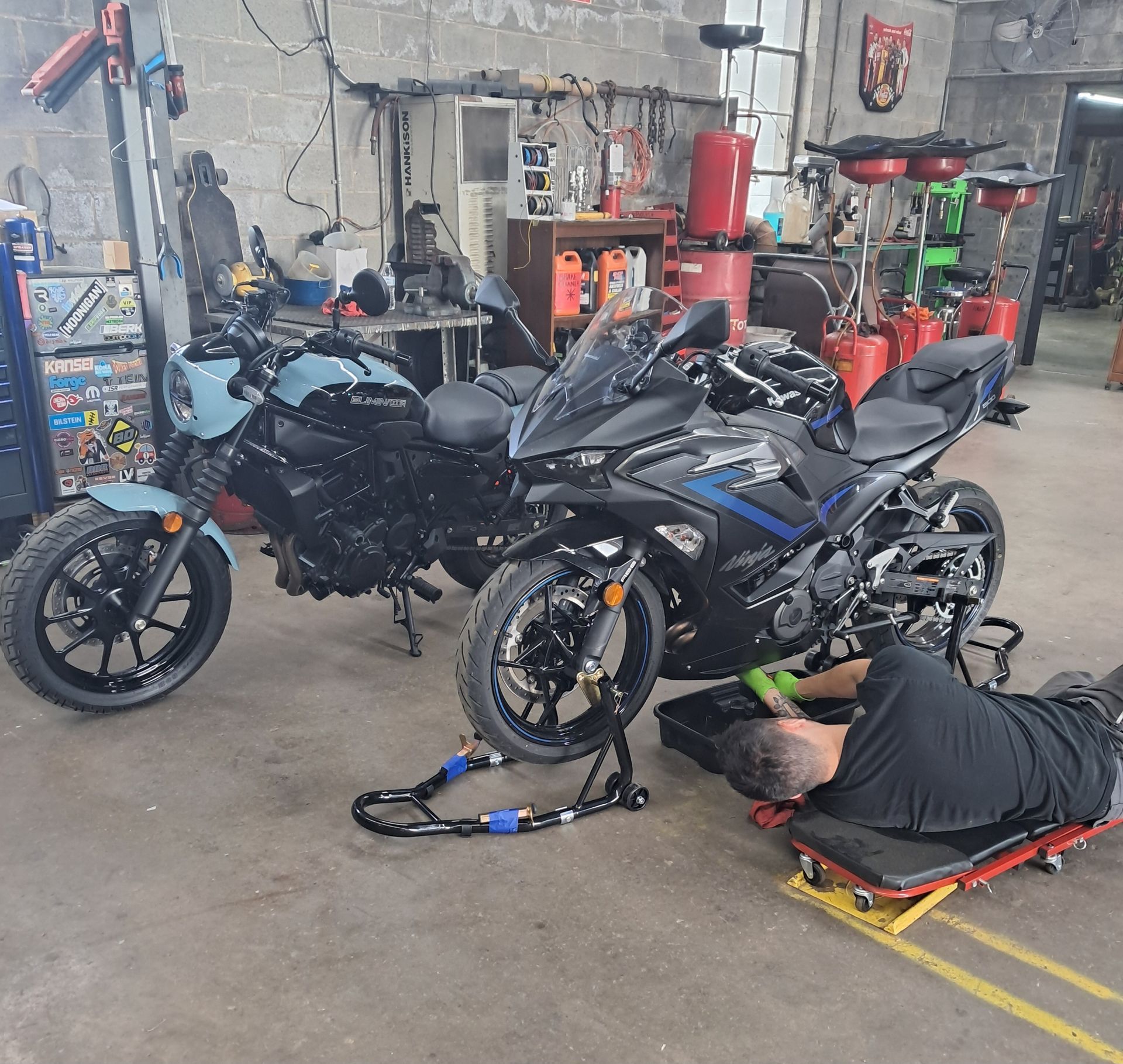 An auto repair shop with a car on a lift, a disassembled car in the foreground.
