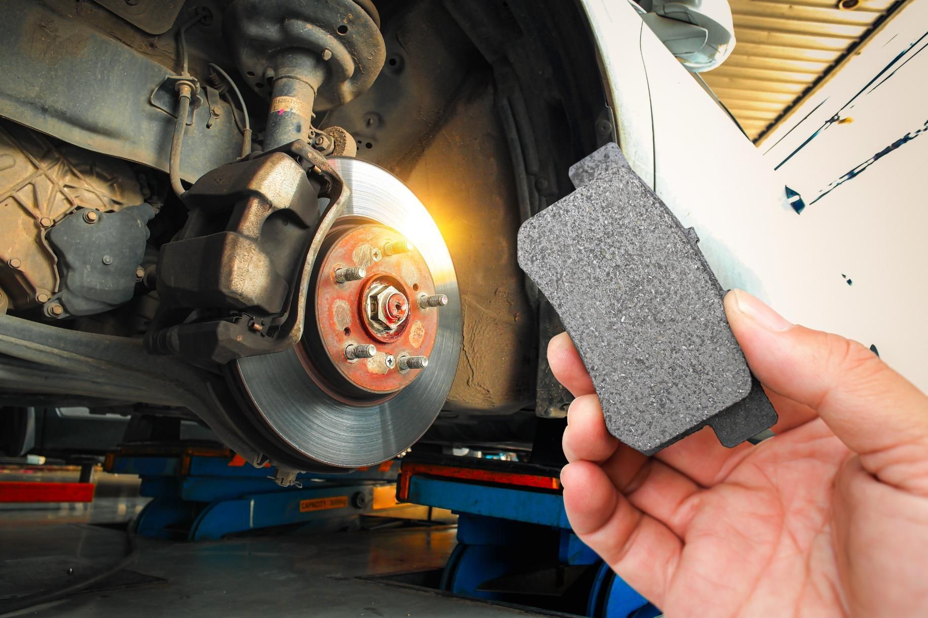A hand holds a new brake pad in front of an automotive brake rotor.