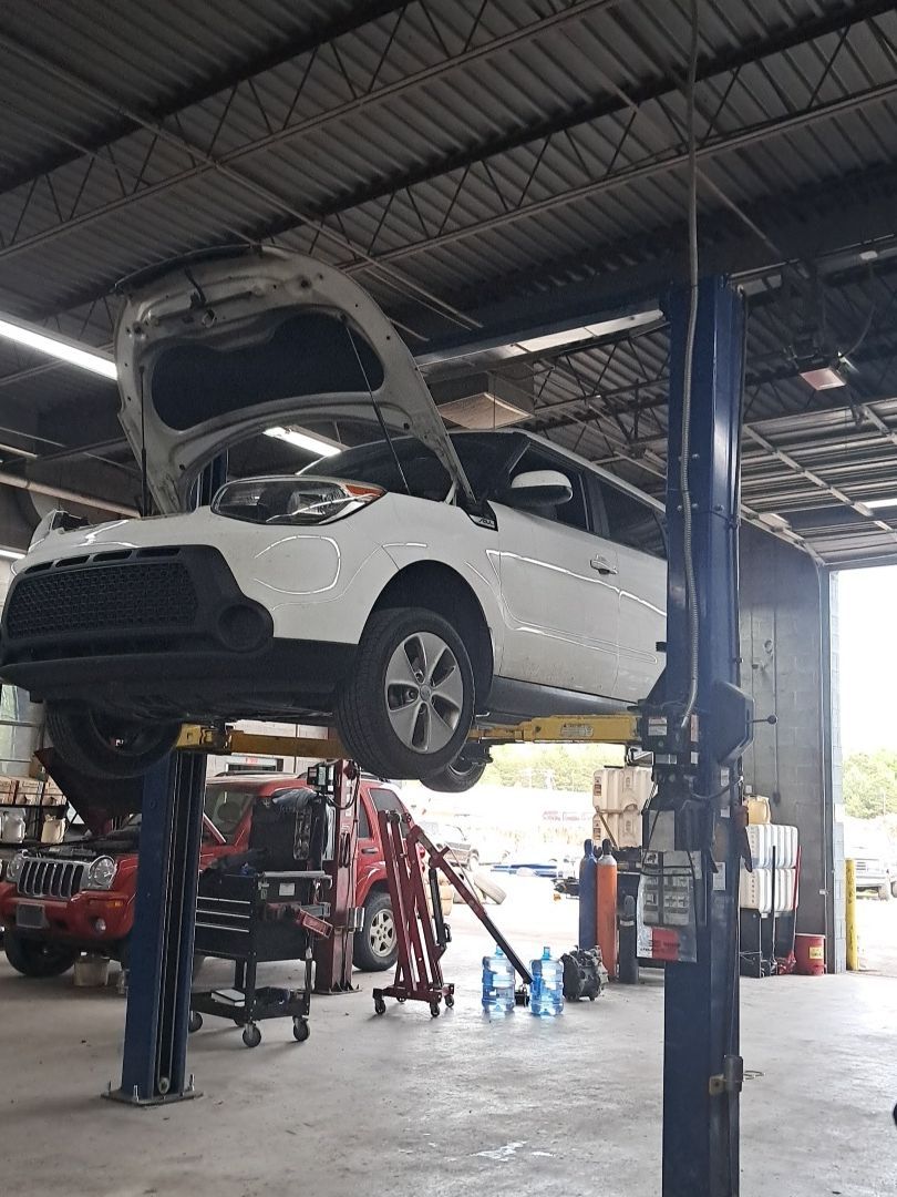 A red sedan with its hood open and wheels removed is raised on a hydraulic lift.