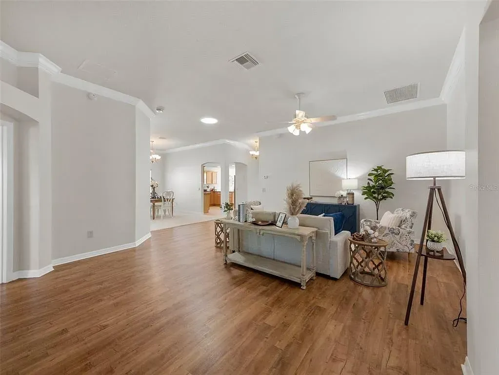 Bright open living room with wood floors, white walls, sofa, lamp, and dining area in back.