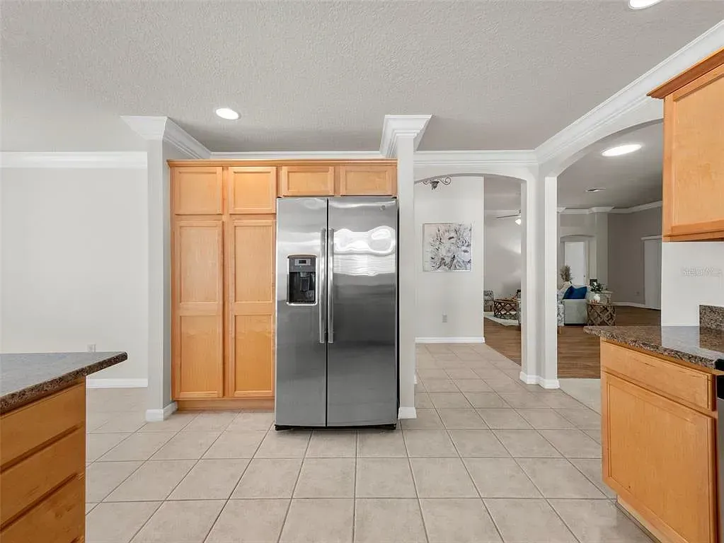 Bright kitchen with stainless steel fridge, wood cabinets, and tiled floor under recessed lights