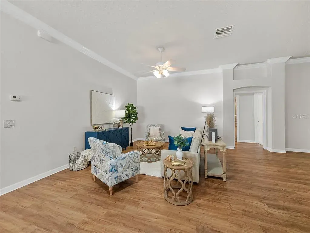 Bright living room with blue floral chairs, blue sofa, wooden floor, and ceiling fan