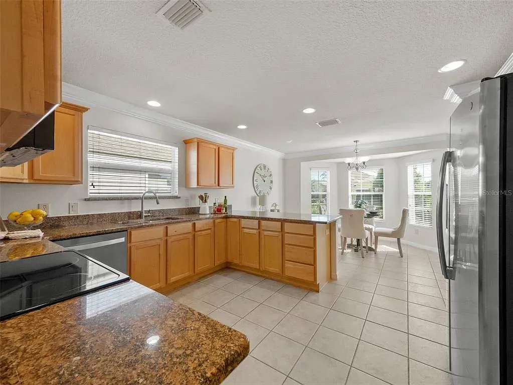 Bright kitchen with wooden cabinets, granite counters, white tile floor, and dining area by sliding glass doors