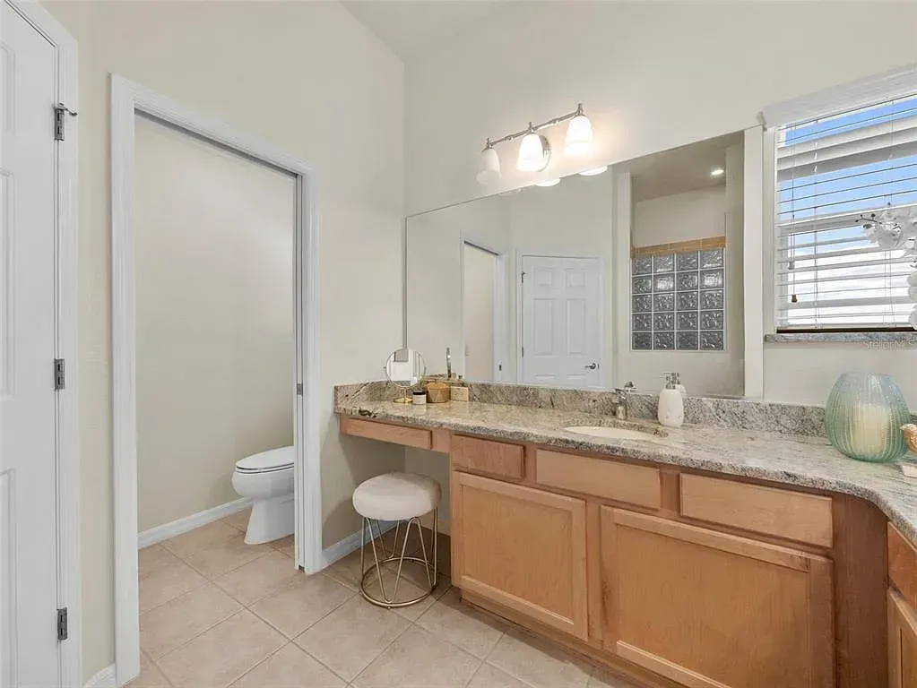 Bright bathroom with double vanity, large mirror, granite countertop, and open toilet area