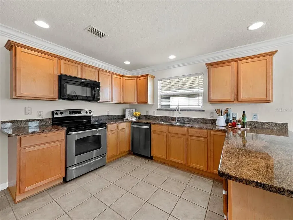 Bright kitchen with wood cabinets, granite counters, stainless stove, and tiled floor