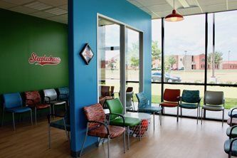 Bright waiting room with colorful chairs, blue and green walls, and large windows overlooking outside.