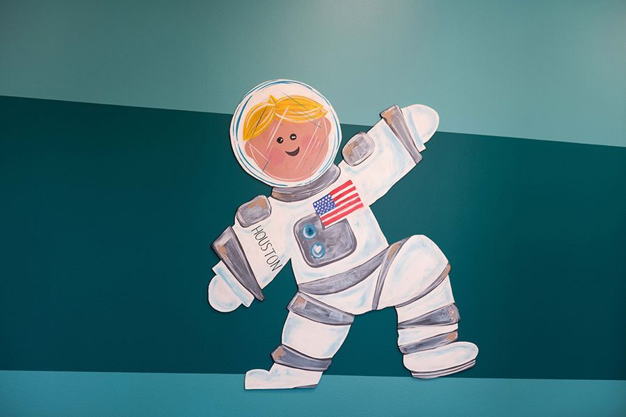 Child in a white astronaut costume waving against a teal background.