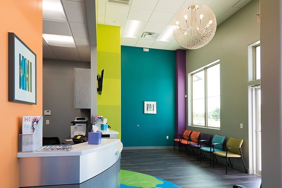 Modern waiting room with colorful walls, chairs by a window, and a reception desk.