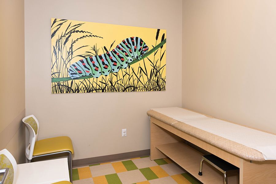 Examination room with treatment table, chair, and colorful abstract wall art.