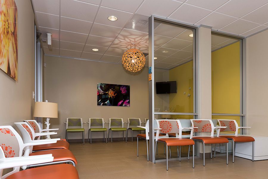 Modern waiting room with orange and white chairs, glass partition, and yellow accent wall