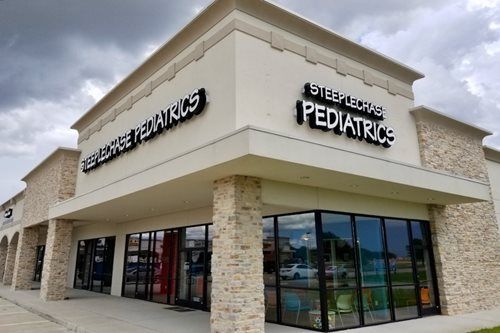 Corner view of a beige pediatric clinic building with large windows and overcast skies