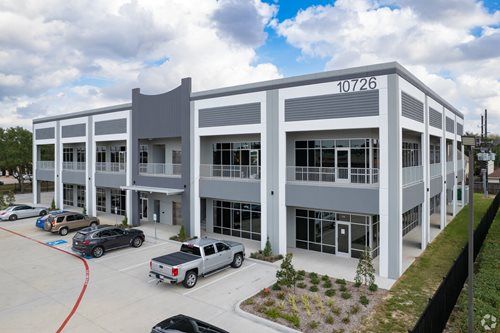 Modern two-story office building with parked vehicles and cloudy sky