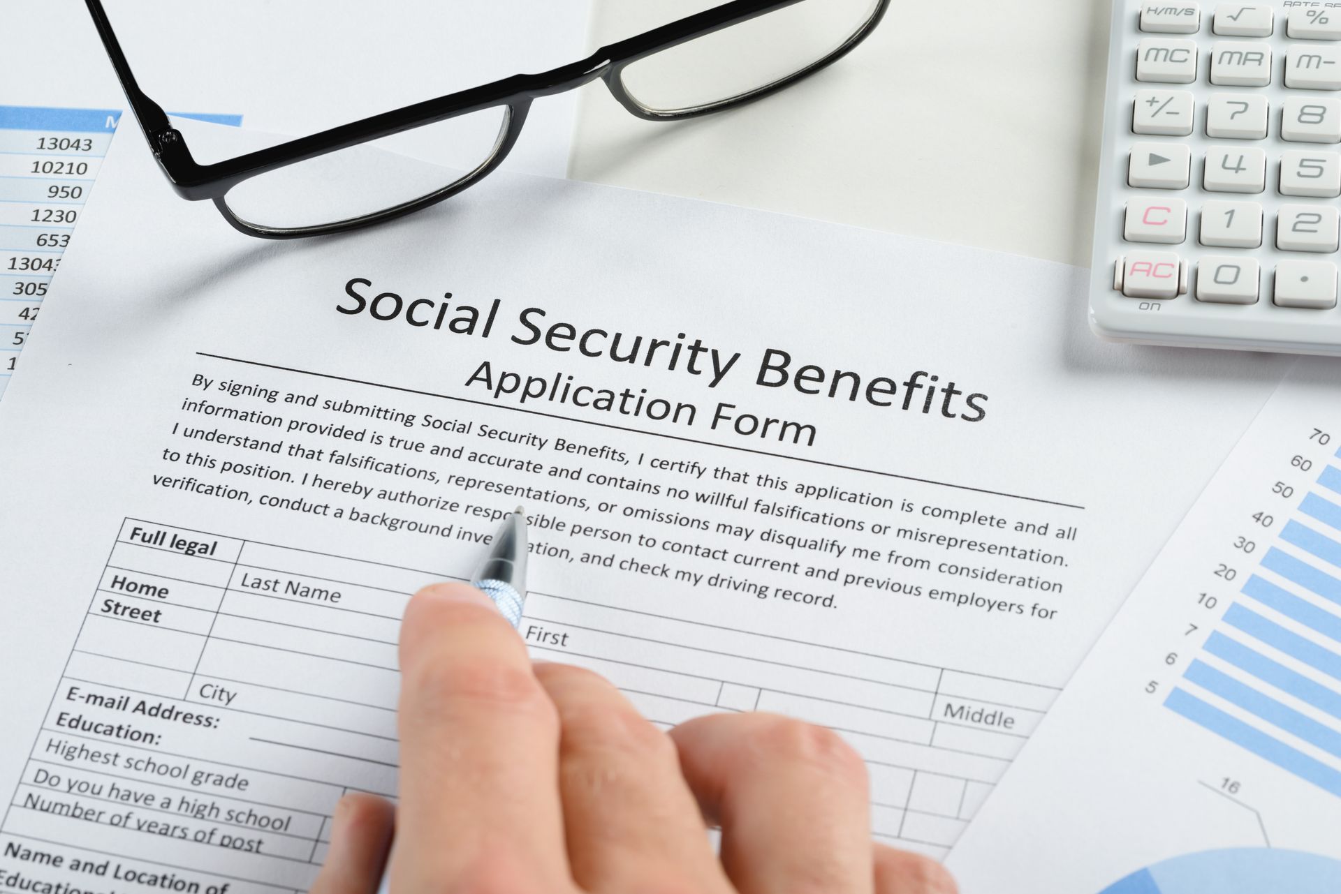 Person filling out a Social Security Benefits application form with pen, calculator, and glasses.