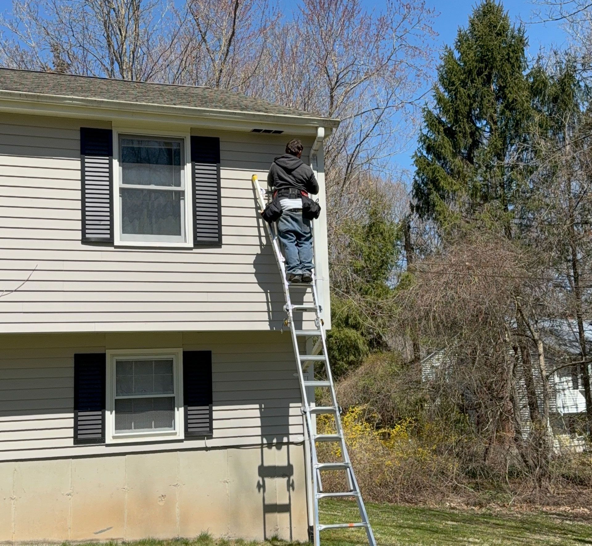 Person on ladder repairing second-story roofline of a gray house