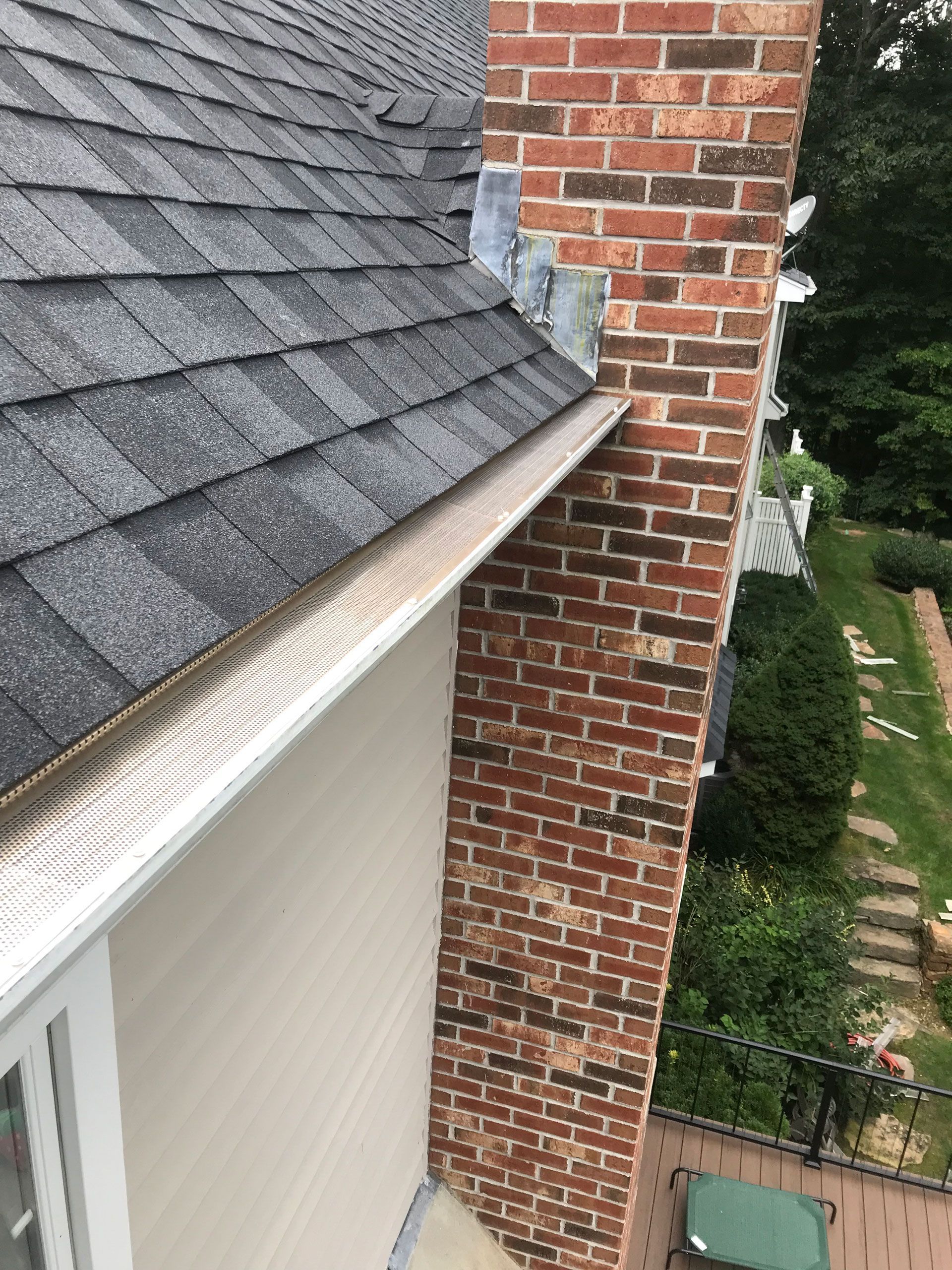 Brick chimney beside a gray shingled roof and white gutter above a house exterior