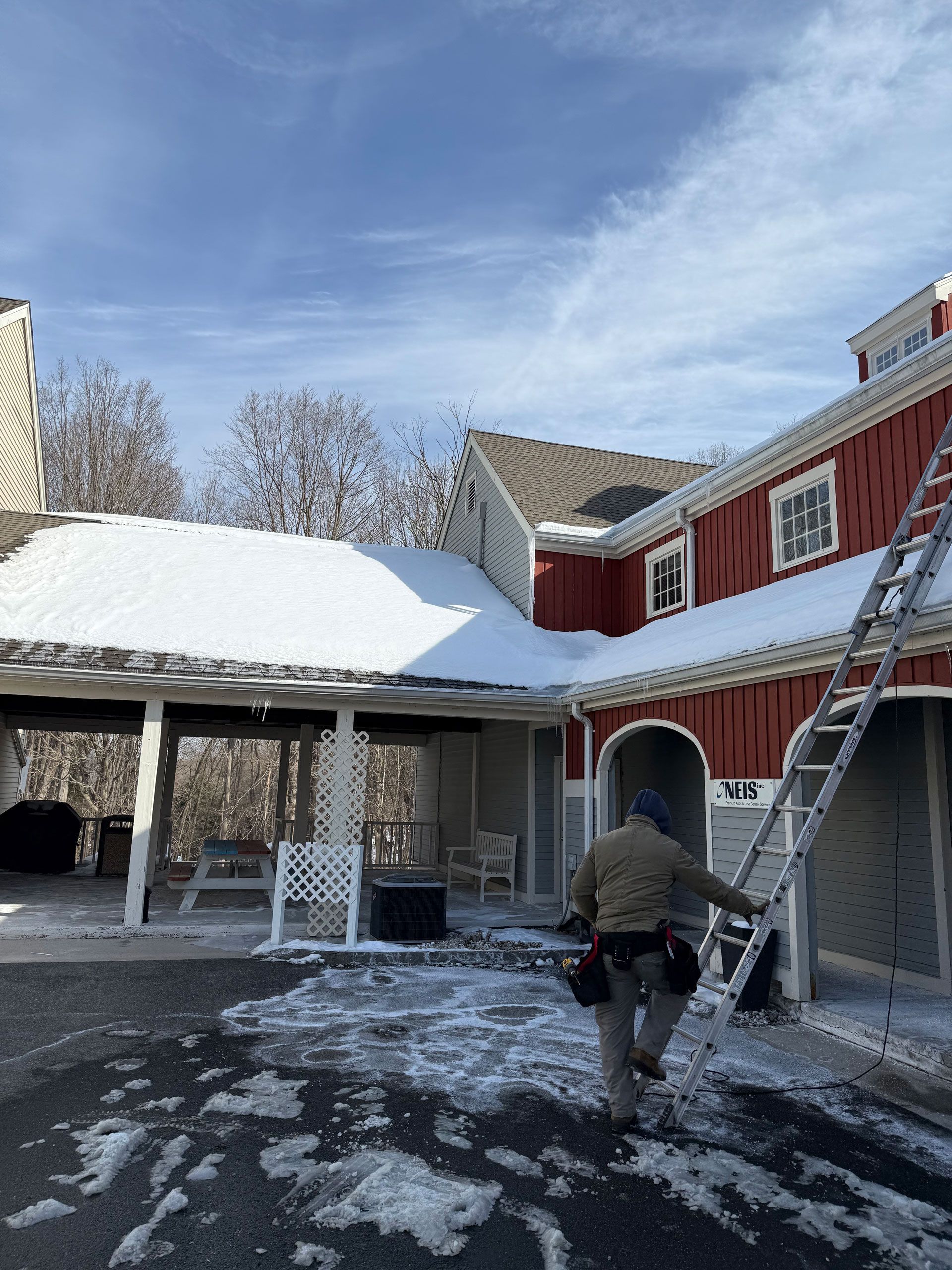 Person walking in a snowy courtyard beside a red building with a ladder leaning against it.