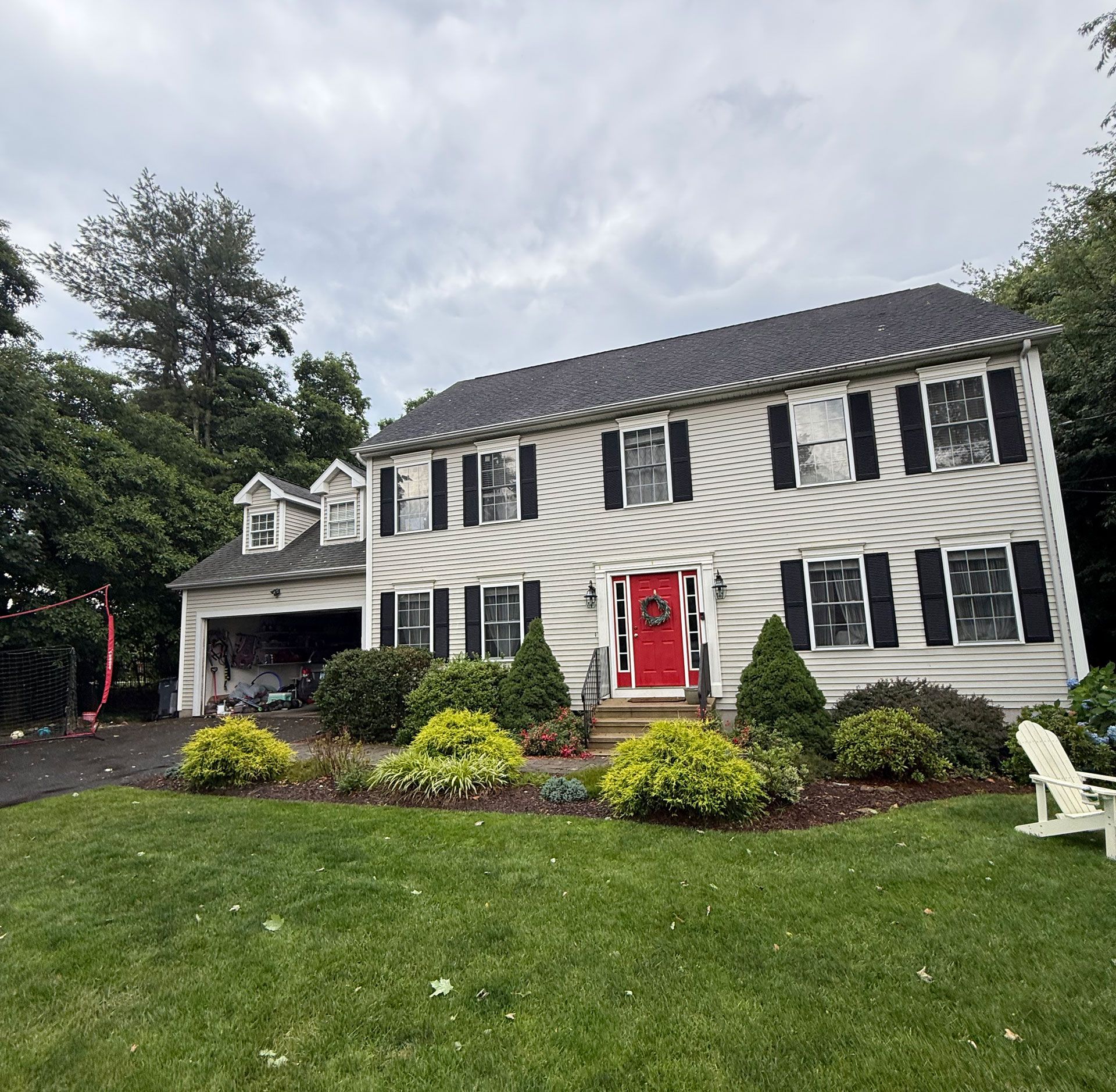 Two-story white house with black shutters, red front door, and landscaped front yard on a cloudy day