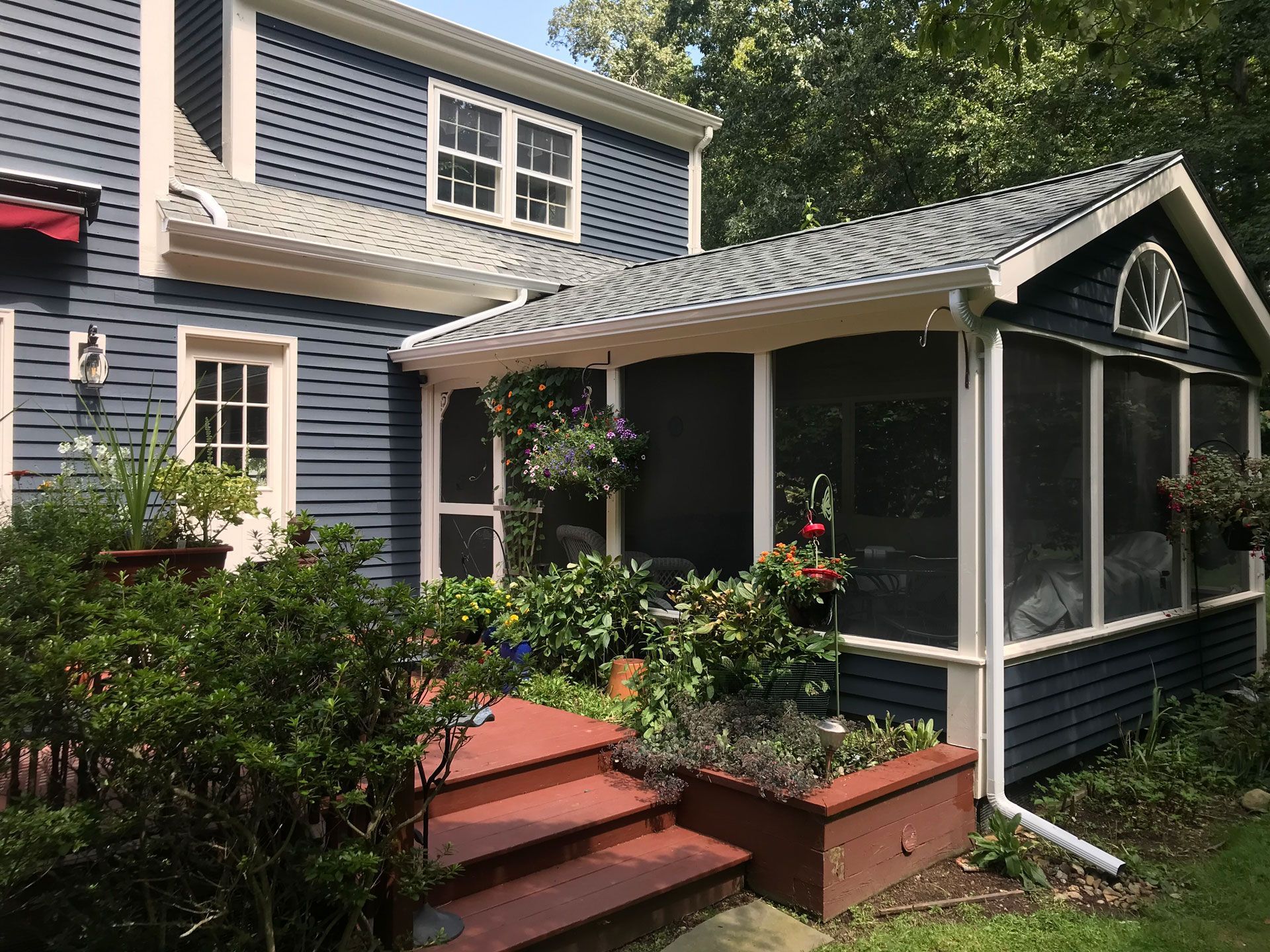 Blue house exterior with screened porch, red steps, and front planters