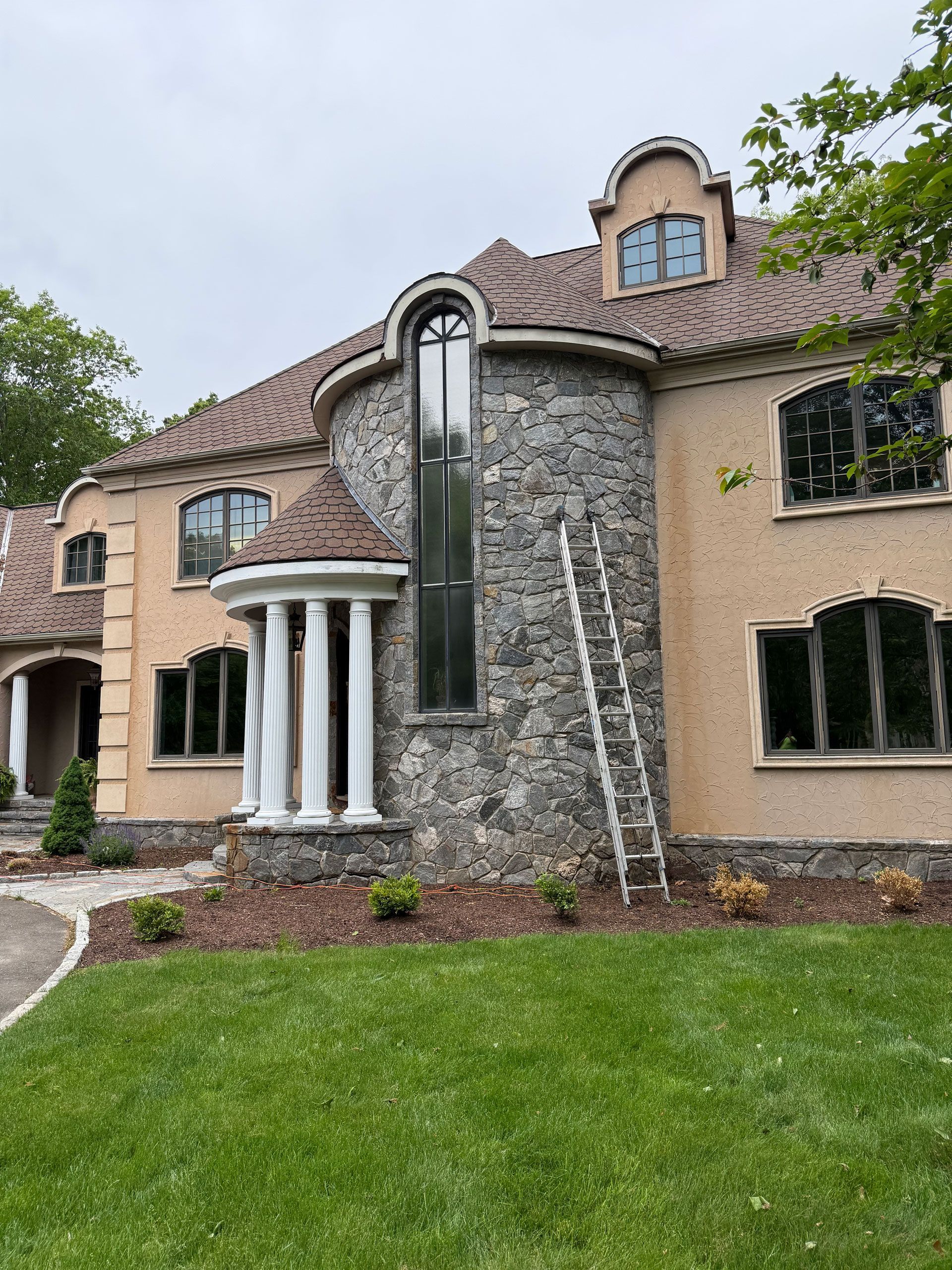 Stucco house with stone facade, arched windows, white columns, and a ladder leaned against the wall.