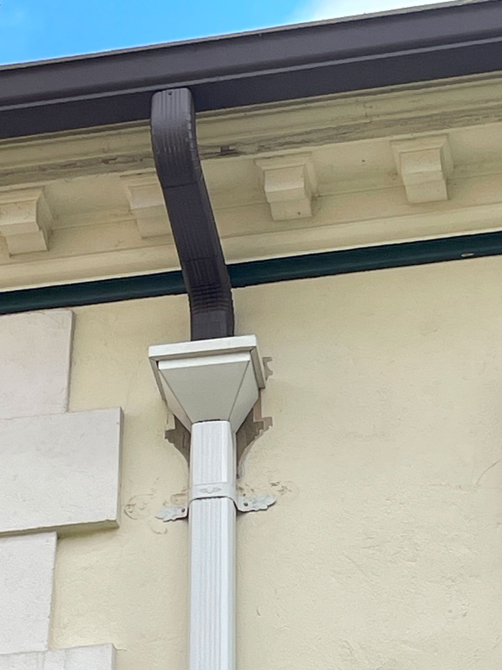 White downspout and black gutter on a cream house exterior under the roof eaves