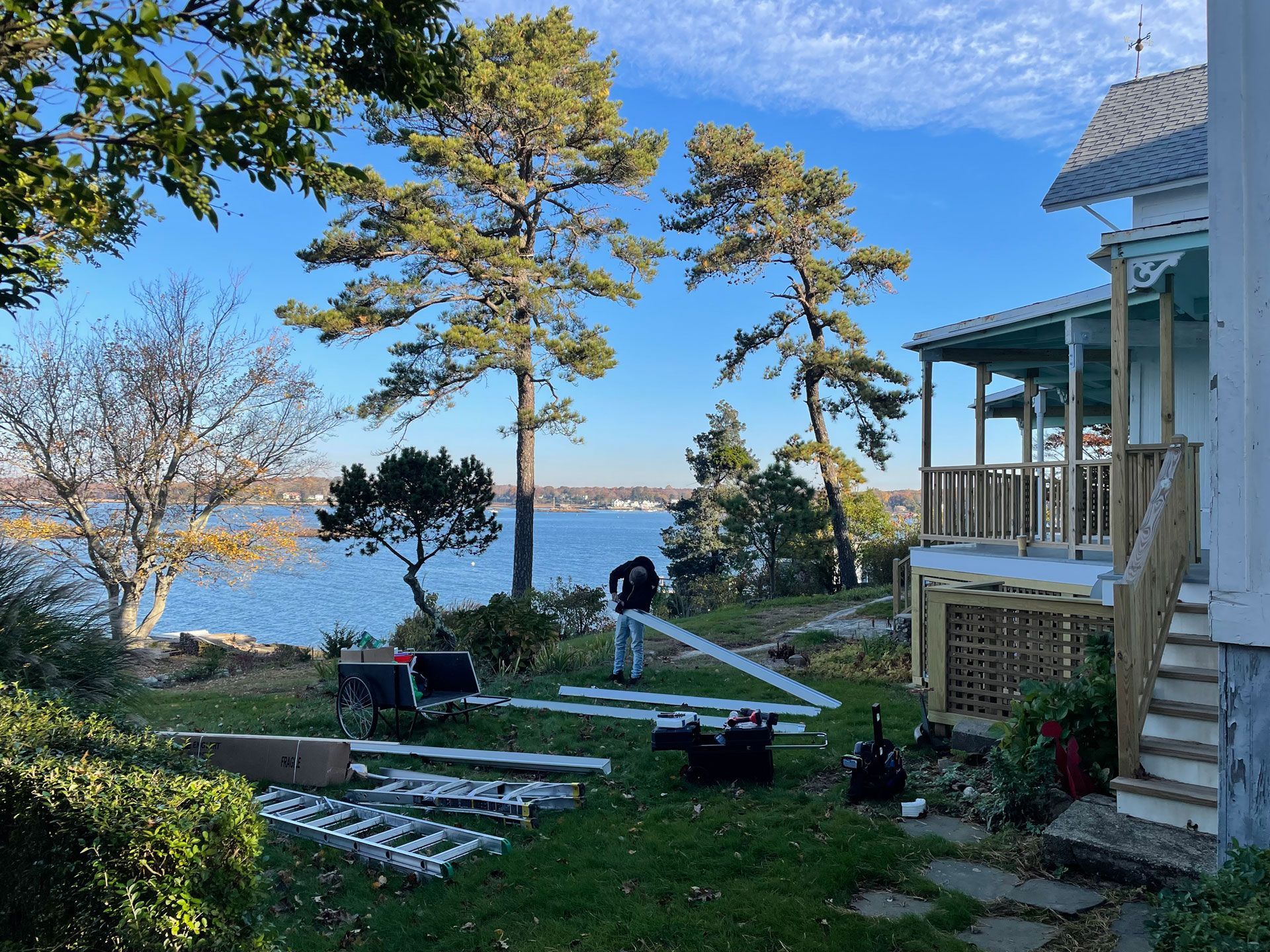 Lakeside backyard with blue house, porch, trees, and ladders laid out on the lawn