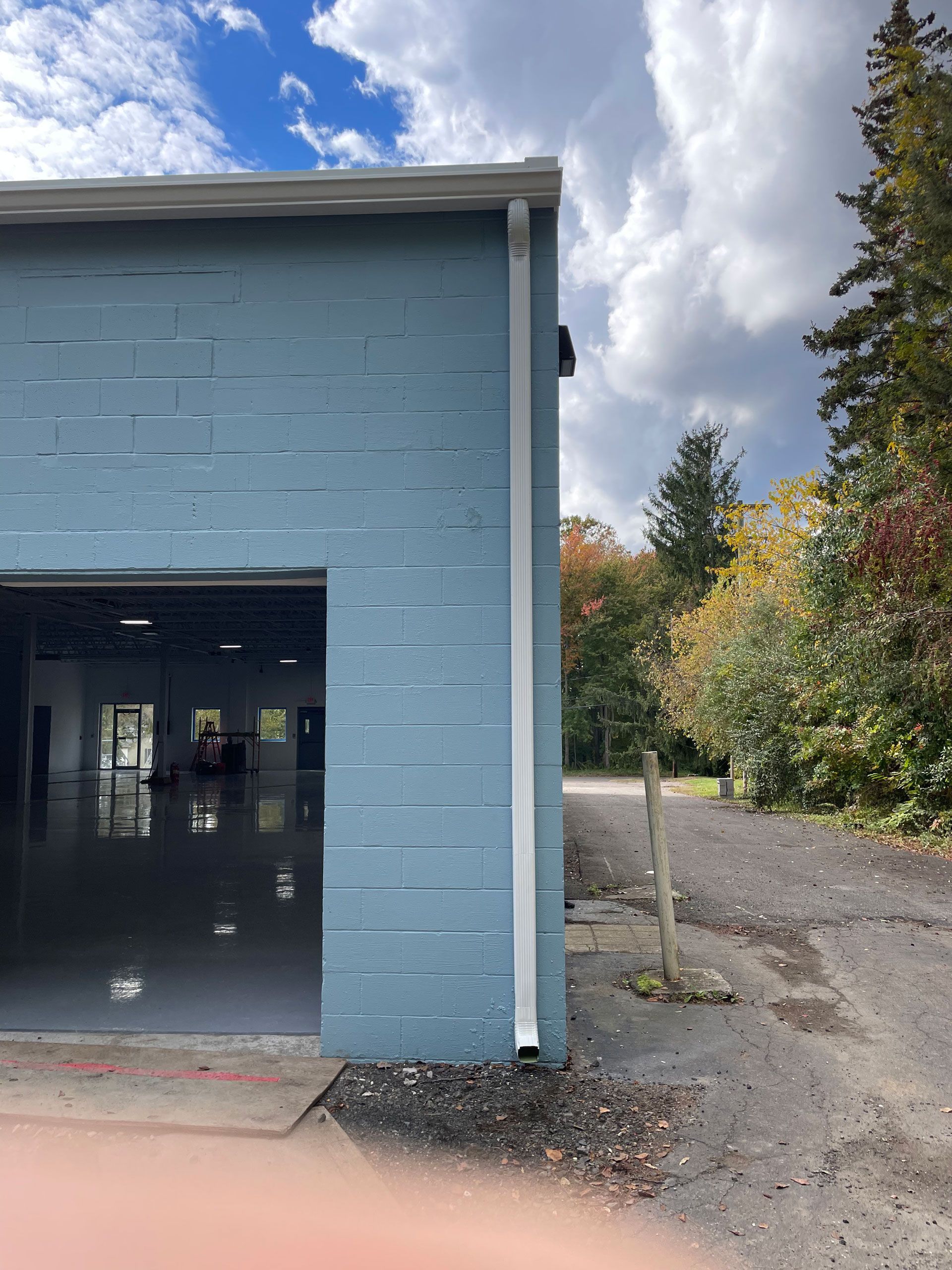 Blue building with open garage bay beside a gravel path and trees under a cloudy sky