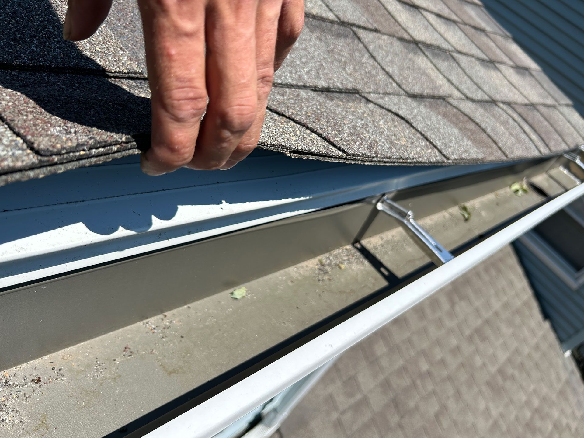 Hand lifting a shingle to reveal roof flashing and gutter repair area